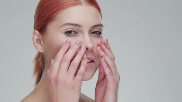 Retrato de estudio de mujer pelirroja joven, hermosa y natural aplicando crema para el cuidado de la piel. Levantamiento facial, cosméticos y maquillaje . — Vídeos de Stock