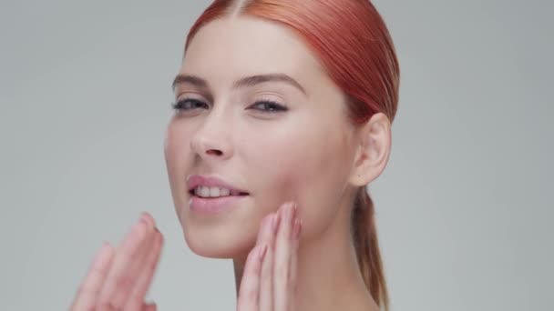 Retrato de estúdio de mulher ruiva jovem, bonita e natural aplicando creme de cuidados da pele. Levantamento facial, cosméticos e maquiagem . — Vídeo de Stock