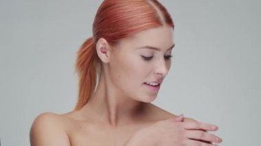 Cilt bakımı kremi süren genç, güzel ve doğal kızıl saçlı kadının stüdyo portresi. Yüz gerdirme, makyaj ve makyaj malzemeleri..