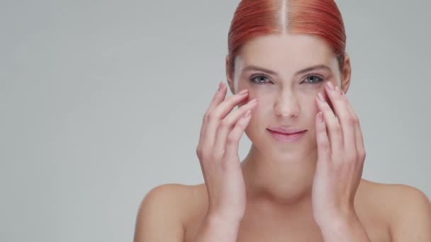 Portrait studio de jeune, belle et naturelle rousse femme appliquant crème de soin de la peau. lifting du visage, cosmétiques et maquillage . — Video