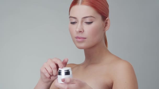 Retrato de estudio de mujer pelirroja joven, hermosa y natural aplicando crema para el cuidado de la piel. Levantamiento facial, cosméticos y maquillaje . — Vídeo de stock