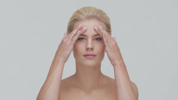Studio portret van jonge, mooie en natuurlijke blonde vrouw die huidverzorgingscrème aanbrengt. Gezichtsheffen, cosmetica en make-up. — Stockvideo