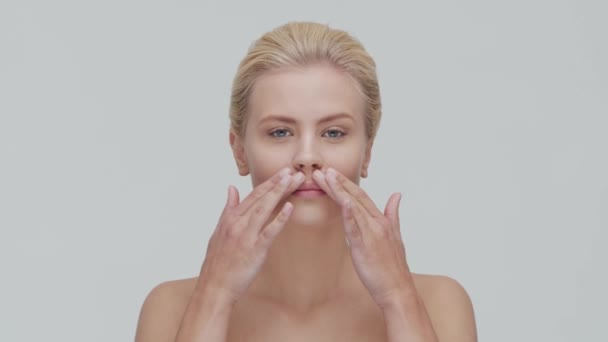 Studioporträt einer jungen, schönen und natürlichen blonden Frau, die Hautpflegecreme aufträgt. Gesichtslifting, Kosmetik und Make-up. — Stockvideo