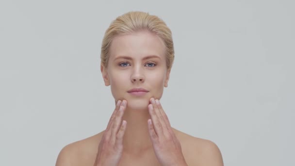 Retrato de estúdio de mulher loira jovem, bonita e natural aplicando creme de cuidados da pele. Levantamento facial, cosméticos e maquiagem . — Vídeo de Stock