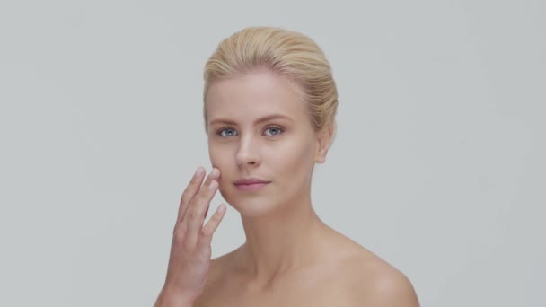 Retrato de estúdio de mulher loira jovem, bonita e natural aplicando creme de cuidados da pele. Levantamento facial, cosméticos e maquiagem . — Vídeo de Stock