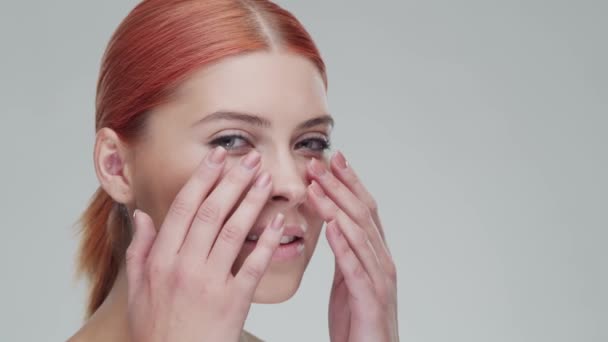 Retrato de estudio de mujer pelirroja joven, hermosa y natural aplicando crema para el cuidado de la piel. Levantamiento facial, cosméticos y maquillaje . — Vídeos de Stock