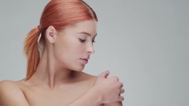 Retrato de estudio de mujer pelirroja joven, hermosa y natural aplicando crema para el cuidado de la piel. Levantamiento facial, cosméticos y maquillaje . — Vídeo de stock