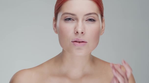 Retrato de estudio de mujer pelirroja joven, hermosa y natural aplicando crema para el cuidado de la piel. Levantamiento facial, cosméticos y maquillaje . — Vídeos de Stock