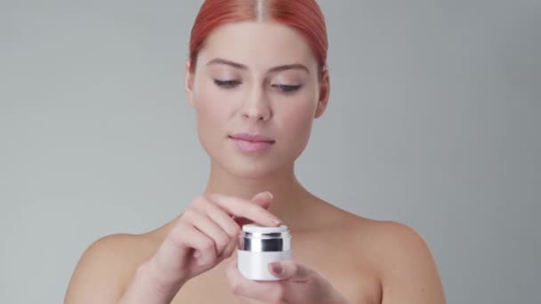 Retrato de estudio de mujer pelirroja joven, hermosa y natural aplicando crema para el cuidado de la piel. Levantamiento facial, cosméticos y maquillaje . — Vídeo de stock