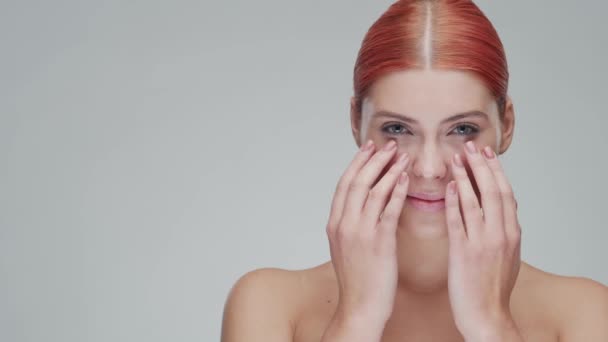 Retrato de estudio de mujer pelirroja joven, hermosa y natural aplicando crema para el cuidado de la piel. Levantamiento facial, cosméticos y maquillaje . — Vídeo de stock