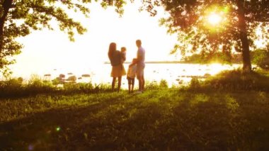 Mutlu bir aile deniz kenarında yürüyor. Kırsal kesimde tarla ve ağaçlar. Gün batımının ya da güneşin sıcacık renkleri. Sevgi dolu ebeveynler ve güzel çocuklar. Sevgi ve ebeveynlik.