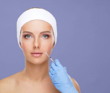 Genç bir kadının güzel yüzüne iğne yapan bir doktor. Estetik ameliyat, cilt gerdirme ve estetik tıp konsepti.