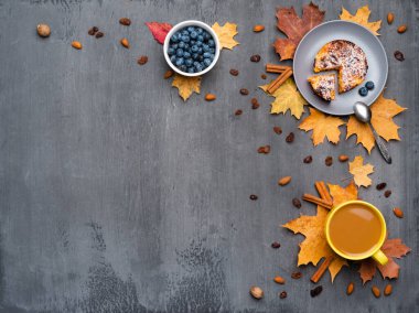 Mevsimlik sonbahar geçmişi. Renkli akçaağaç yaprakları ve bir fincan sıcak içecek, kahve, latte veya kapuçino, hindistan cevizi, kek, yabanmersini ve tarçın..