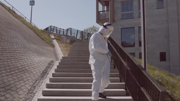 防護服の男は防腐スプレーで通りを消毒します コロナウイルスCovid 19疾患による表面処理 ウイルスのパンデミックと保護の概念 — ストック動画