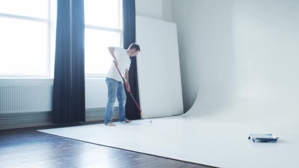 ローラーペインターとホワイトペイントを使用した写真スタジオでの若い男の絵画サイクロラマ — ストック動画