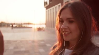 Dışarıda bankta oturan çekici genç bir iş kadını. Video kaset için akıllı telefon kullanan bir kız. Sosyal uzaklık kavramı. Gün batımı ışığı.