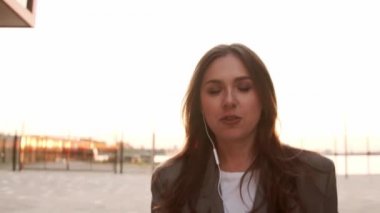 Genç ve çekici bir iş kadını dışarıda yürüyor ve telefon görüşmesi yapıyor. Gün batımı ışığı.