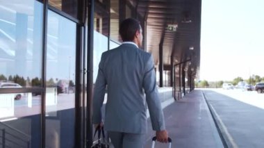 Zarif bir işadamı havaalanı boyunca bavuluyla yürüyor. Formalite icabı genç bir postacı. İş gezisi ve seyahat kavramları.