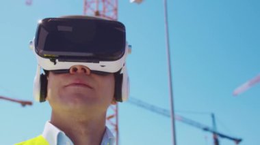 İnşaat alanının önünde sanal gerçeklik teknolojileri kullanarak VR kasklı profesyonel bir inşaatçı. Ofis binası ve vinç arka planı. Emlak ve yatırım kavramları