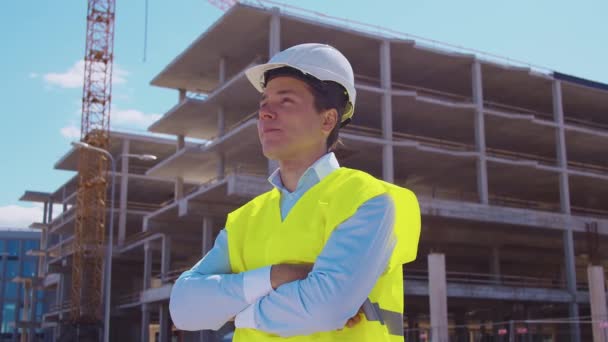 专业建筑商站在建筑工地前 头戴安全帽 身穿背心的工头 办公大楼和起重机背景 房地产和投资概念 — 图库视频影像