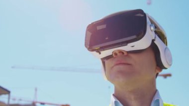 İnşaat alanının önünde sanal gerçeklik teknolojileri kullanarak VR kasklı profesyonel bir inşaatçı. Ofis binası ve vinç arka planı. Emlak ve yatırım kavramları