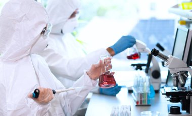 Laboratuvarda çalışan koruyucu giysi ve maskeli bilim adamları laboratuvar ekipmanları kullanıyorlardı: mikroskop, test tüpleri. Biyolojik tehlike, farmasötik keşif, bakteri ve virüs bilimi kavramı.