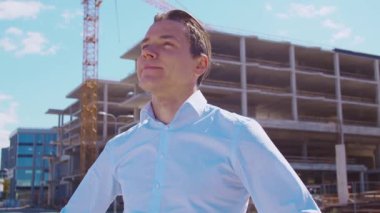 İnşaat alanının önünde duran bir iş adamı. Ofis binası ve vinç arka planı. Geliştirme, emlak ve yatırım kavramları.
