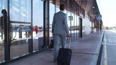 Zarif bir işadamı havaalanı boyunca bavuluyla yürüyor. Formalite icabı genç bir postacı. İş gezisi ve seyahat kavramları.