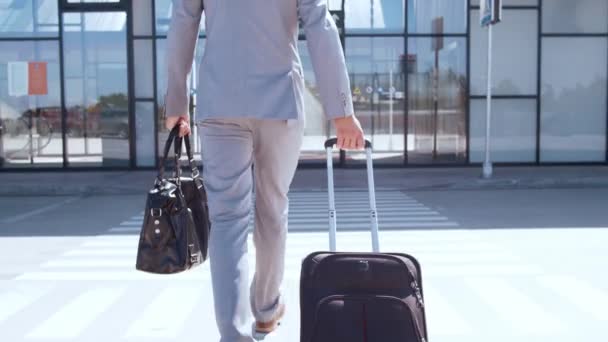 空港に沿ってスーツケースを持つエレガントなビジネスマン歩く フォーマルウェアの若いメール起業家 旅行のコンセプト — ストック動画