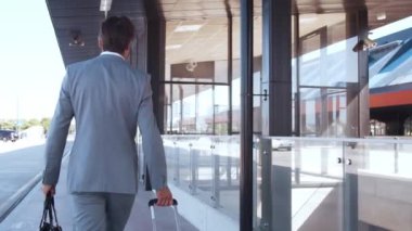 Zarif bir işadamı havaalanı boyunca bavuluyla yürüyor. Formalite icabı genç bir postacı. İş gezisi ve seyahat kavramları.