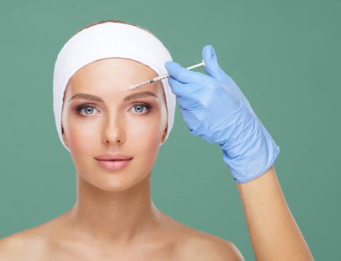 Genç bir kadının güzel yüzüne iğne yapan bir doktor. Estetik ameliyat, cilt gerdirme ve estetik tıp konsepti.