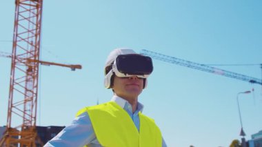 İnşaat alanının önünde sanal gerçeklik teknolojileri kullanarak VR kasklı profesyonel bir inşaatçı. Ofis binası ve vinç arka planı. Emlak ve yatırım kavramları