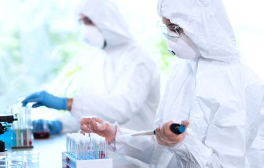 Laboratuvarda çalışan koruyucu giysi ve maskeli bilim adamları laboratuvar ekipmanları kullanıyorlardı: mikroskop, test tüpleri. Biyolojik tehlike, farmasötik keşif, bakteri ve virüs bilimi kavramı.