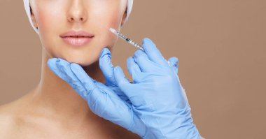 Genç bir kadının güzel yüzüne iğne yapan bir doktor. Estetik ameliyat, cilt gerdirme ve estetik tıp konsepti.