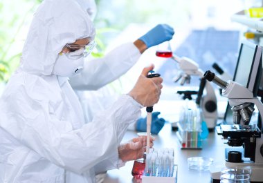Laboratuvarda çalışan koruyucu giysi ve maskeli bilim adamları laboratuvar ekipmanları kullanıyorlardı: mikroskop, test tüpleri. İlaç, enfeksiyon ve aşı keşfi kavramı.