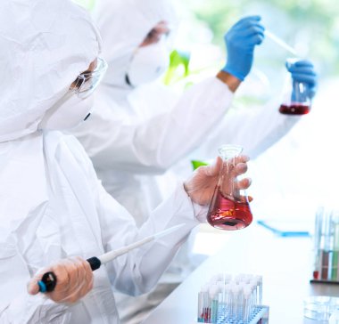 Laboratuvarda çalışan koruyucu giysi ve maskeli bilim adamları laboratuvar ekipmanları kullanıyorlardı: mikroskop, test tüpleri. Biyolojik tehlike, farmasötik keşif, bakteri ve virüs bilimi kavramı.