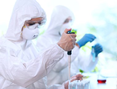 Laboratuvarda çalışan koruyucu giysi ve maskeli bilim adamları laboratuvar ekipmanları kullanıyorlardı: mikroskop, test tüpleri. Biyolojik tehlike, farmasötik keşif, bakteri ve virüs bilimi kavramı.