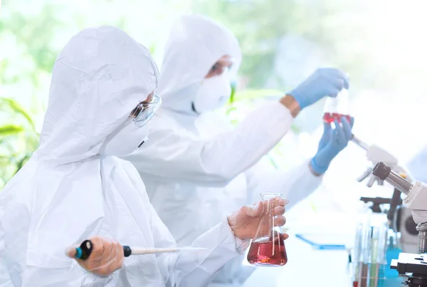 Scientists in protection suits and masks working in research lab using laboratory equipment: microscopes, test tubes. Medicine, infection and vaccine discovery concept.