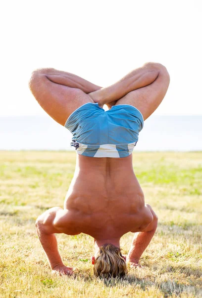 健康英俊的男人在草地上练习瑜伽 背景是大海和天空 日落时的伸展运动 保健和生活方式概念 — 图库照片