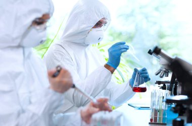 Laboratuvarda çalışan koruyucu giysi ve maskeli bilim adamları laboratuvar ekipmanları kullanıyorlardı: mikroskop, test tüpleri. İlaç, enfeksiyon ve aşı keşfi kavramı.