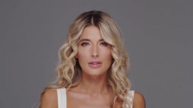 Gri arka planda genç, güzel ve anlamlı sarışın bir kadının stüdyo portresi..