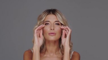 Gri arka planda genç, güzel ve anlamlı sarışın bir kadının stüdyo portresi..