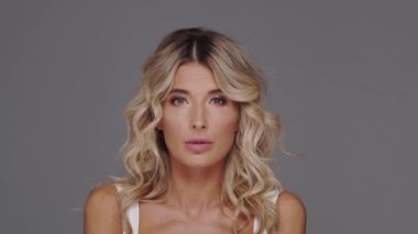 Gri arka planda genç, güzel ve anlamlı sarışın bir kadının stüdyo portresi..