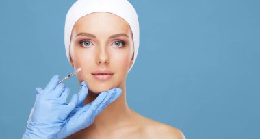 Genç bir kadının güzel yüzüne iğne yapan bir doktor. Estetik ameliyat, cilt gerdirme ve estetik tıp konsepti.