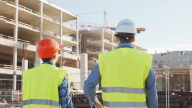 İnşaat alanının önünde duran profesyonel inşaatçılar. Ustabaşı ve inşaat mühendisi. Ofis binası ve vinç arka planı. İş, gayrimenkul ve yatırım kavramları.