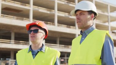 İnşaat alanının önünde duran profesyonel inşaatçılar. Ustabaşı ve inşaat mühendisi. Ofis binası ve vinç arka planı. İş, gayrimenkul ve yatırım kavramları.