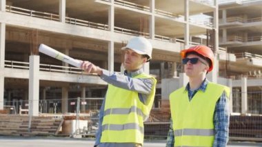 İnşaat alanının önünde duran profesyonel inşaatçılar. Ustabaşı ve inşaat mühendisi. Ofis binası ve vinç arka planı. İş, gayrimenkul ve yatırım kavramları.