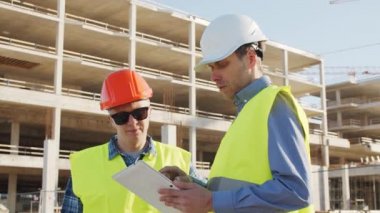 İnşaat alanının önünde duran profesyonel inşaatçılar. Ustabaşı ve inşaat mühendisi. Ofis binası ve vinç arka planı. İş, gayrimenkul ve yatırım kavramları.