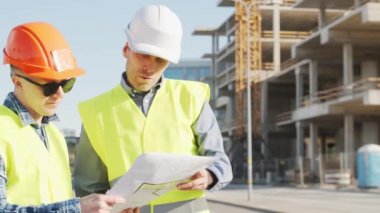İnşaat alanının önünde duran profesyonel inşaatçılar. Ustabaşı ve inşaat mühendisi. Ofis binası ve vinç arka planı. İş, gayrimenkul ve yatırım kavramları.