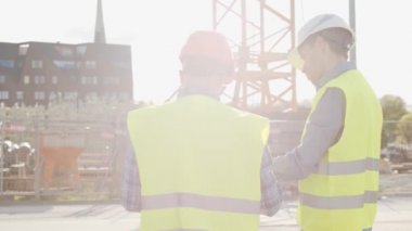 İnşaat alanının önünde duran profesyonel inşaatçılar. Ustabaşı ve inşaat mühendisi. Ofis binası ve vinç arka planı. İş, gayrimenkul ve yatırım kavramları.